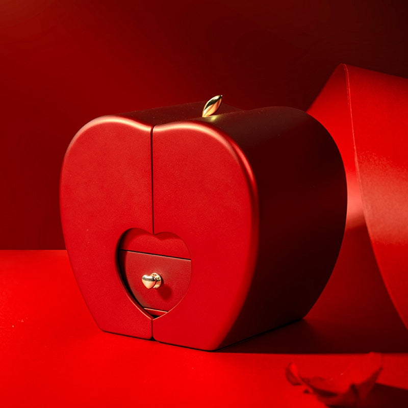 Closed red apple-shaped keepsake gift box with a gold clasp, photographed against a red background