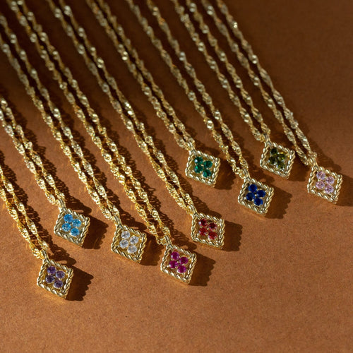 The full birthstone necklace range laid out on terracotta — twelve gold rope-framed pendants, each set with four crystals in a different month's colour