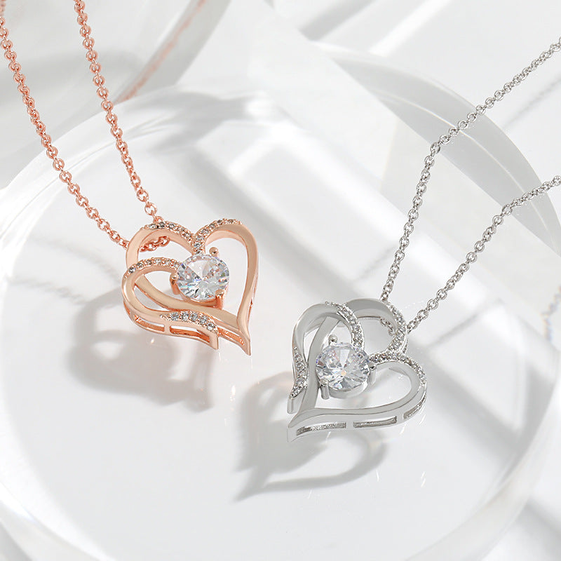Both finishes of the double heart necklace, rose gold and silver, arranged on a pale ceramic dish