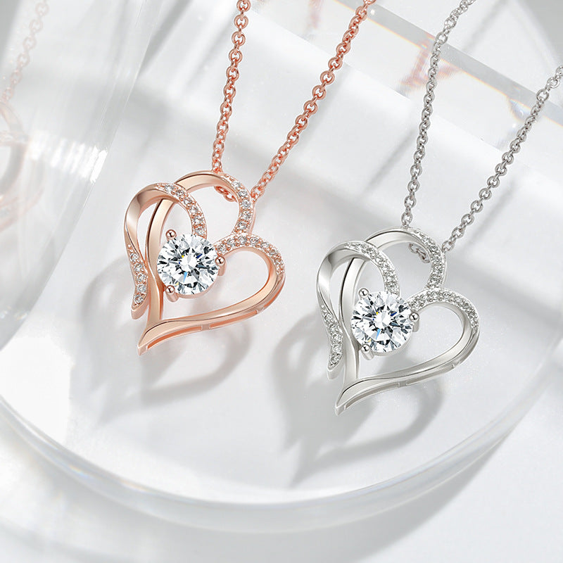 Rose gold and silver double heart pendant necklaces laid side by side on a pale dish