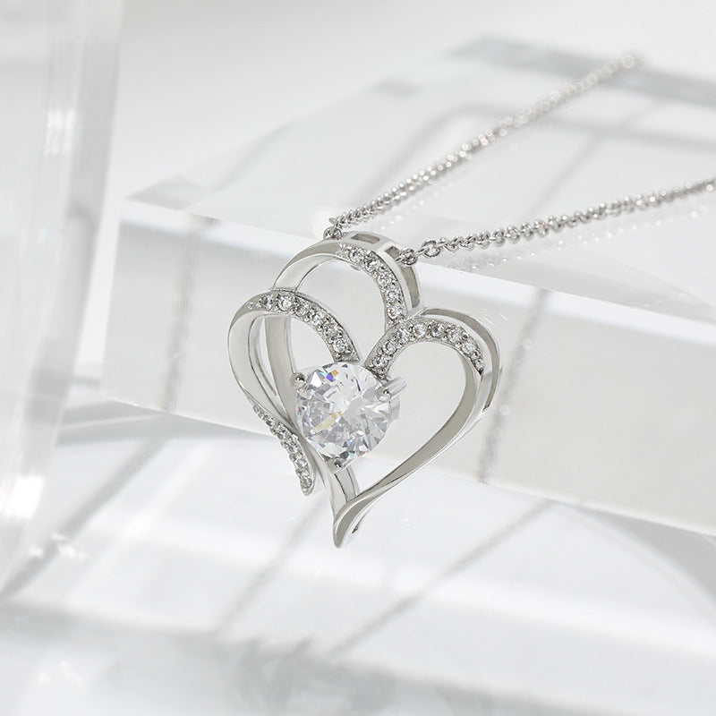 Silver double heart pendant resting against clear glass in soft daylight